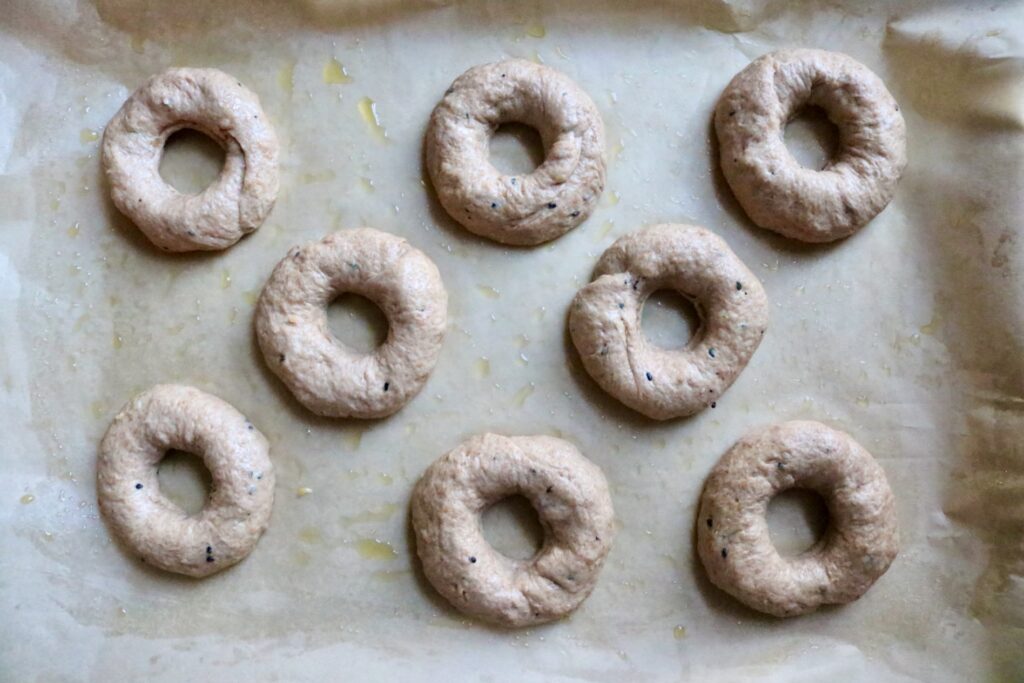 raw whole grain everything bagels lined up on baking sheet
