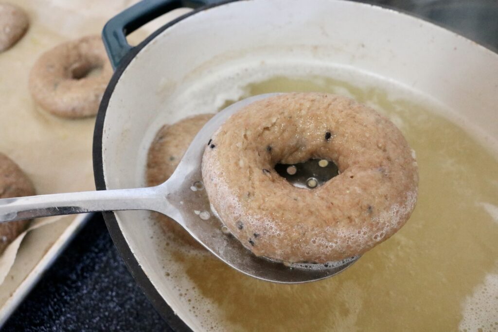draining whole grain everything bagel with slotted spoon
