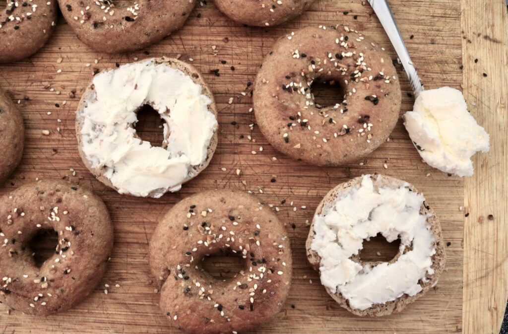 whole grain everything bagels laying on countertop two have cream cheese on them