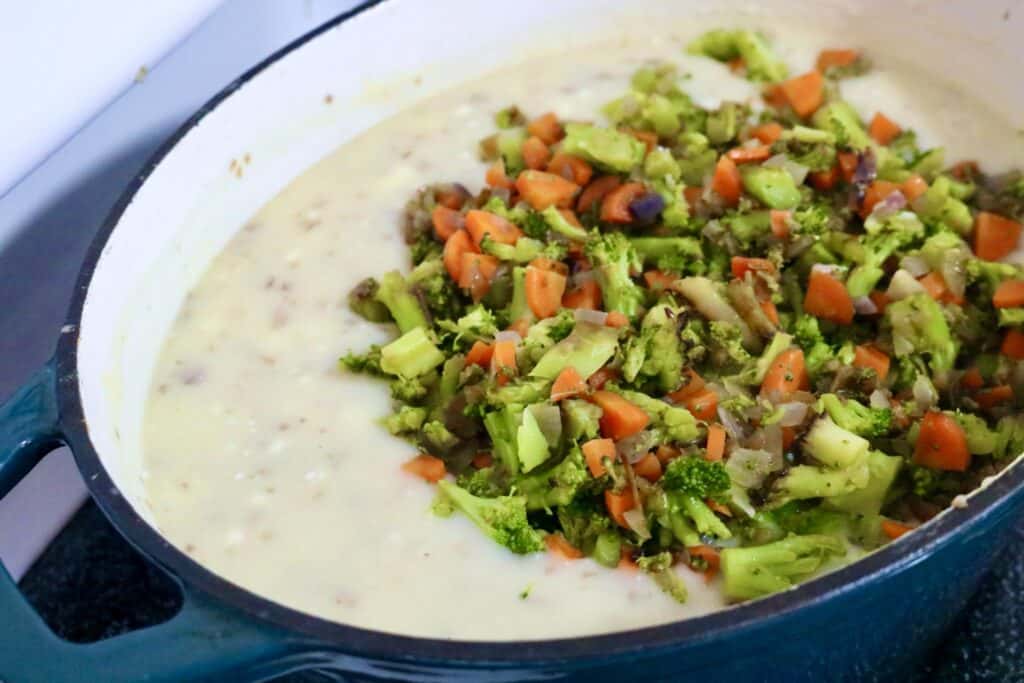 Creamy potato vegetable soup in pot with sauteed vegetables on top