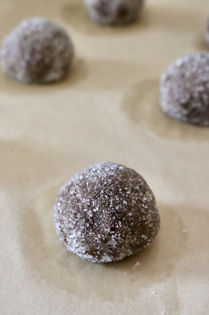 sourdough whole grain molasses cookie dough balls coated in sugar on parchment lined baking sheet