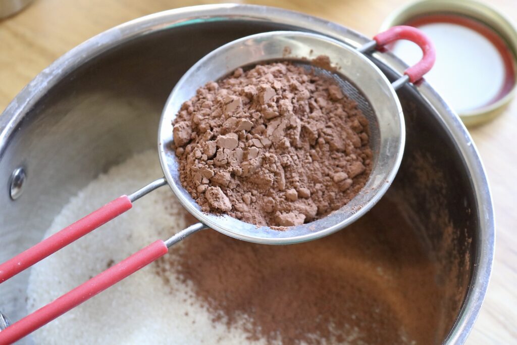 sifting cocoa powder into a saucepan with sugar in it