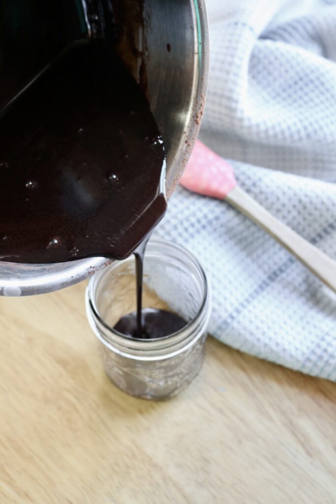 pouring mocha sauce into a half pint jar with a small spatula and tea towel beside it