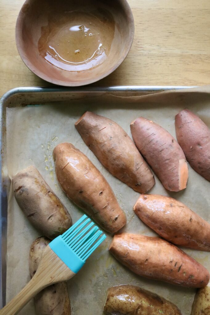 potatoes on a parchment paper lined baking sheet with olive oil in a wooden bowl and a pastry brush