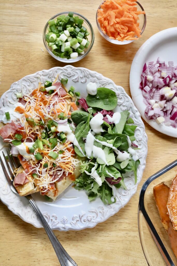 baked potato with toppings and a salad on a plate with bowls of vegetable around it
