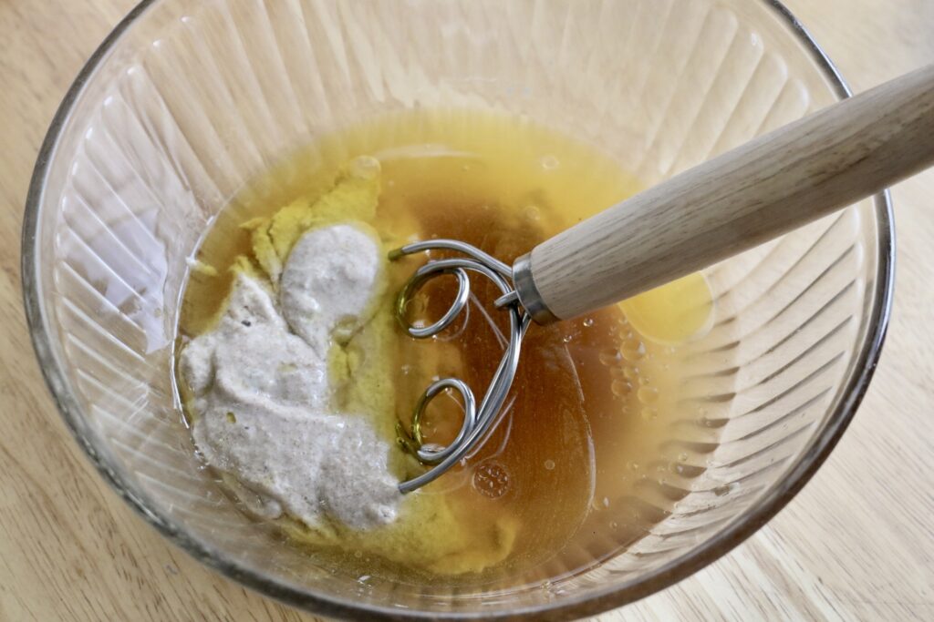 water, sugar, and starter in bowl with a whisk