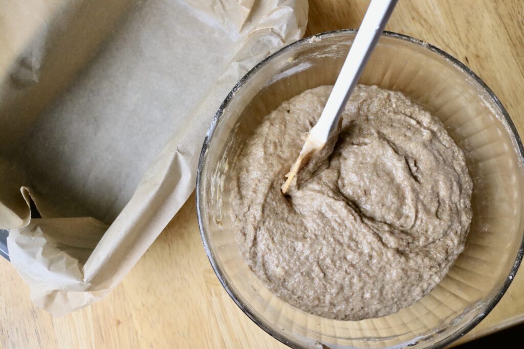 bowl of batter next to parchment paper lined bread pan