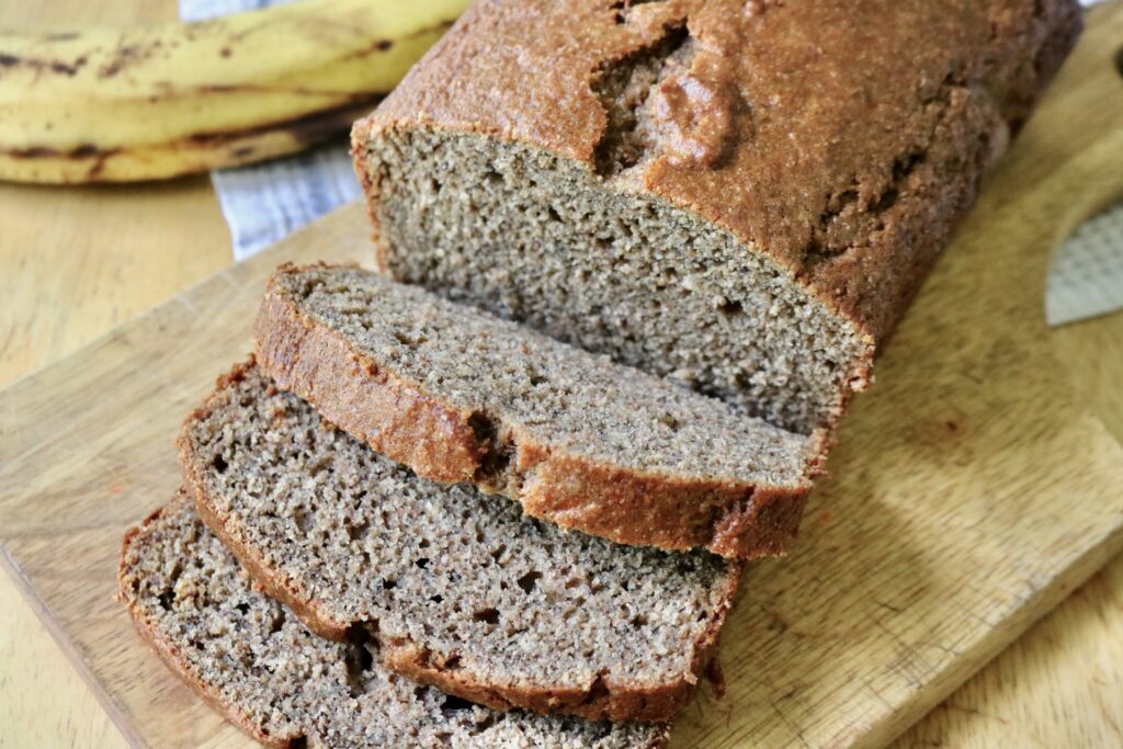 sourdough discard banana bread slices on a cutting board next to loaf