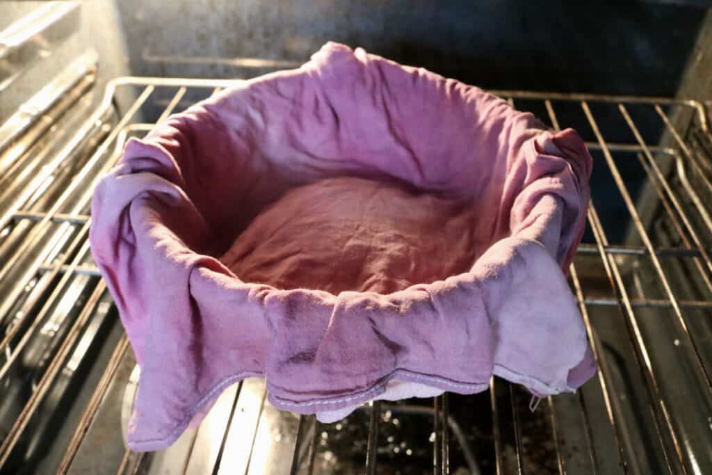 bowl of dough covered with a tea towel in the oven with the light on