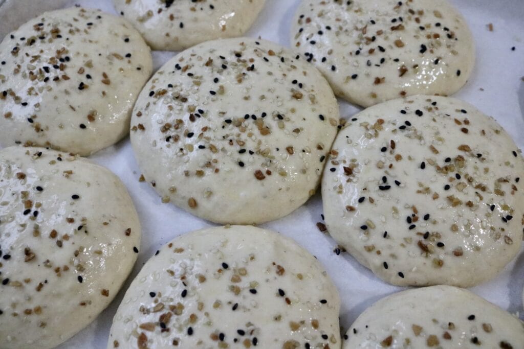uncooked buns on a baking sheet with seeds sprinkled on them